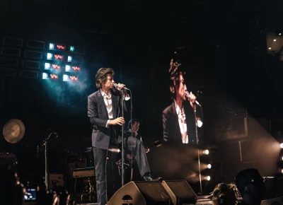 The front man for Arctic Monkeys performing with a projection of himself to the right.