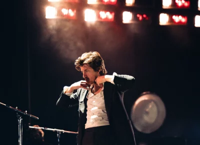Arctic Monkey's Alex Turner adjusting his shirt collar and chain.