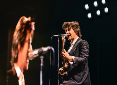 Alex Turner singing and playing an electric guitar, with a projection of himself in the background.