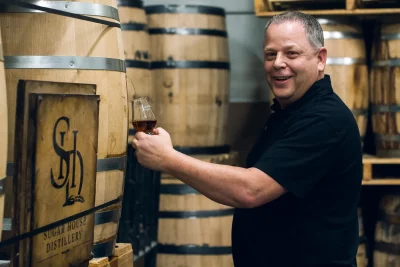 James Fowler of Sugar House Distillery stands with a glass among barrels of whiskey.