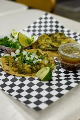 Tacos sit on checkered paper with garnish and limes at Street Tacos.