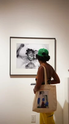 A person in a green baseball hat viewing a black and white photo framed on the wall.