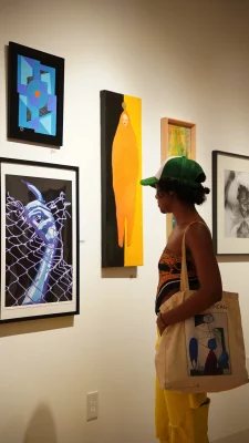 A gallery-goer in a green hat enjoying a framed painting.