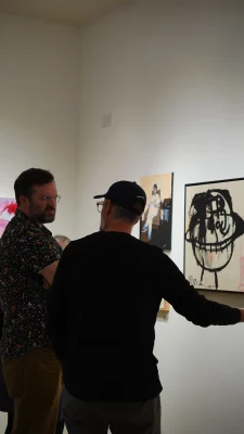 Two attendees stand and discuss the art on the wall.