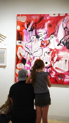 A young child and their parent viewing a large abstract painting.