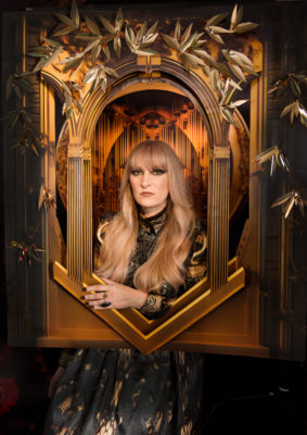 Rebecca Vernon of The Keening stands in a golden frame wearing a black dress