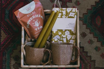 A gift box with two mugs, two olive green candles, tea and a tea towel at Atelier.