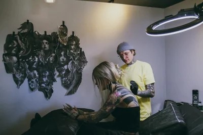Bobby Johnson tattoos a woman's back in his studio with a black mural behind him.