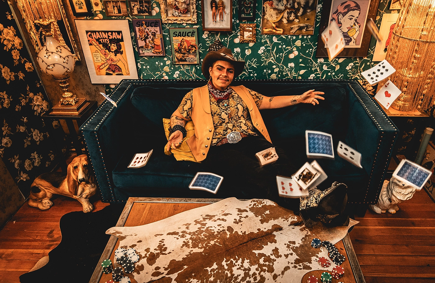 Heller Highwater leans across a sofa surrounded by playing cards and a cow skin rug.