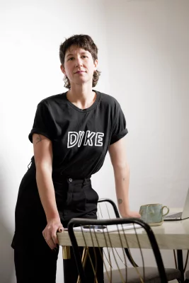 Amanda Madden leans on a table, wearing a shirt that reads "Dyke."