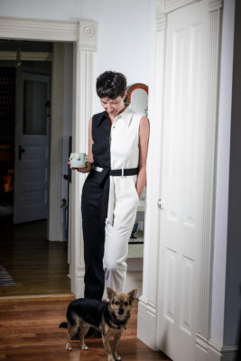 Amanda Madden looks down at their dog while wearing a half-black-half-white jumpsuit.
