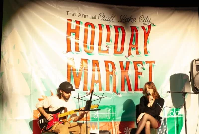 A singer and a guitar player on stage in front of a Holiday Market banner.