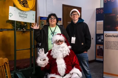 Two volunteers stand with Santa Claus.