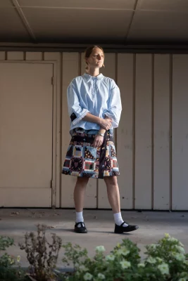 Abigail Rue Jenson looks away in front of a building wearing a boxy blue blouse and wrap skirt she designed.