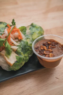 Spring rolls next to a cup of peanut sauce.