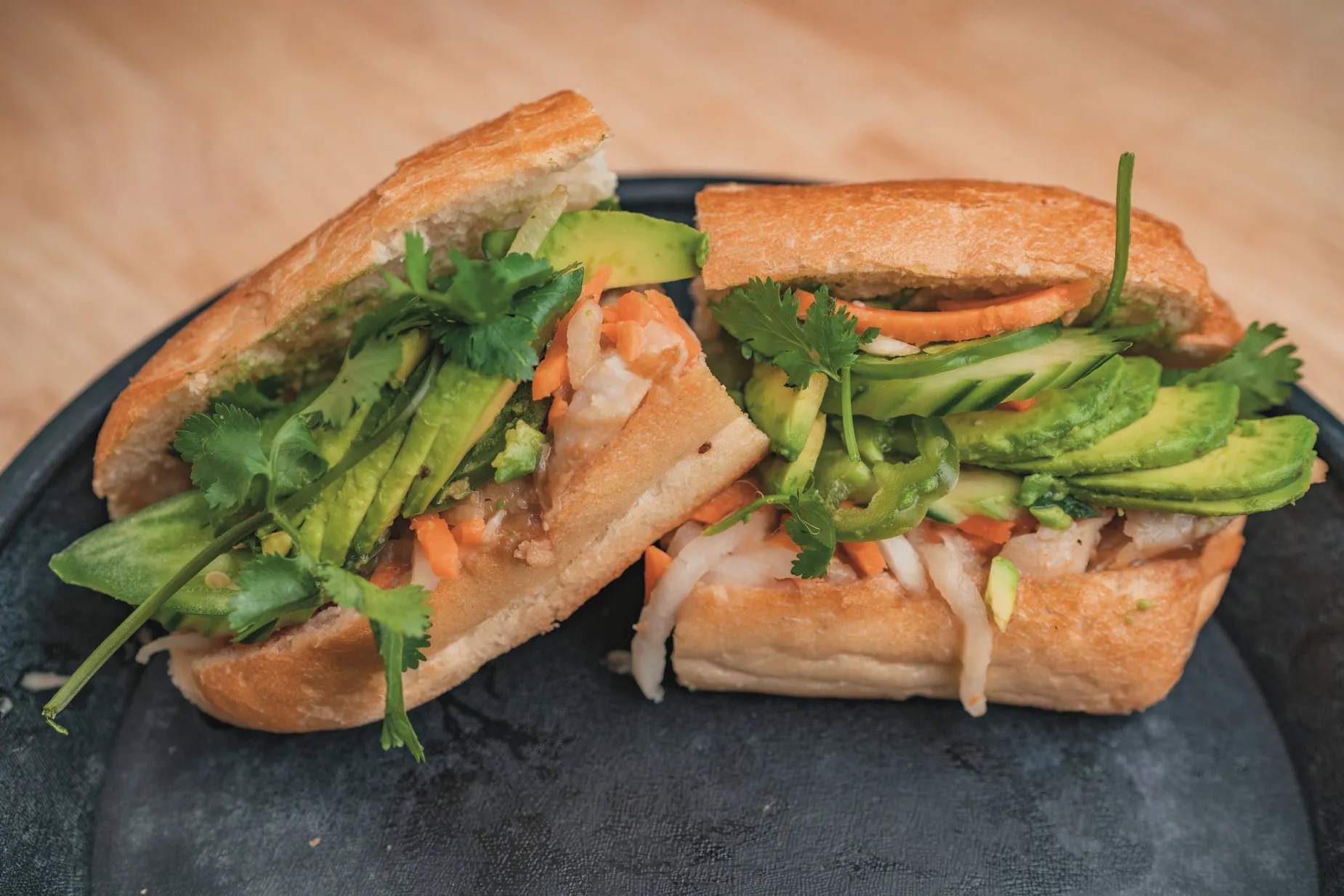 A banh mi loaded with avocado and vegetables.