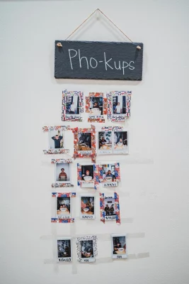 A white wall of photos under a hanging sign that reads "Pho-kups."