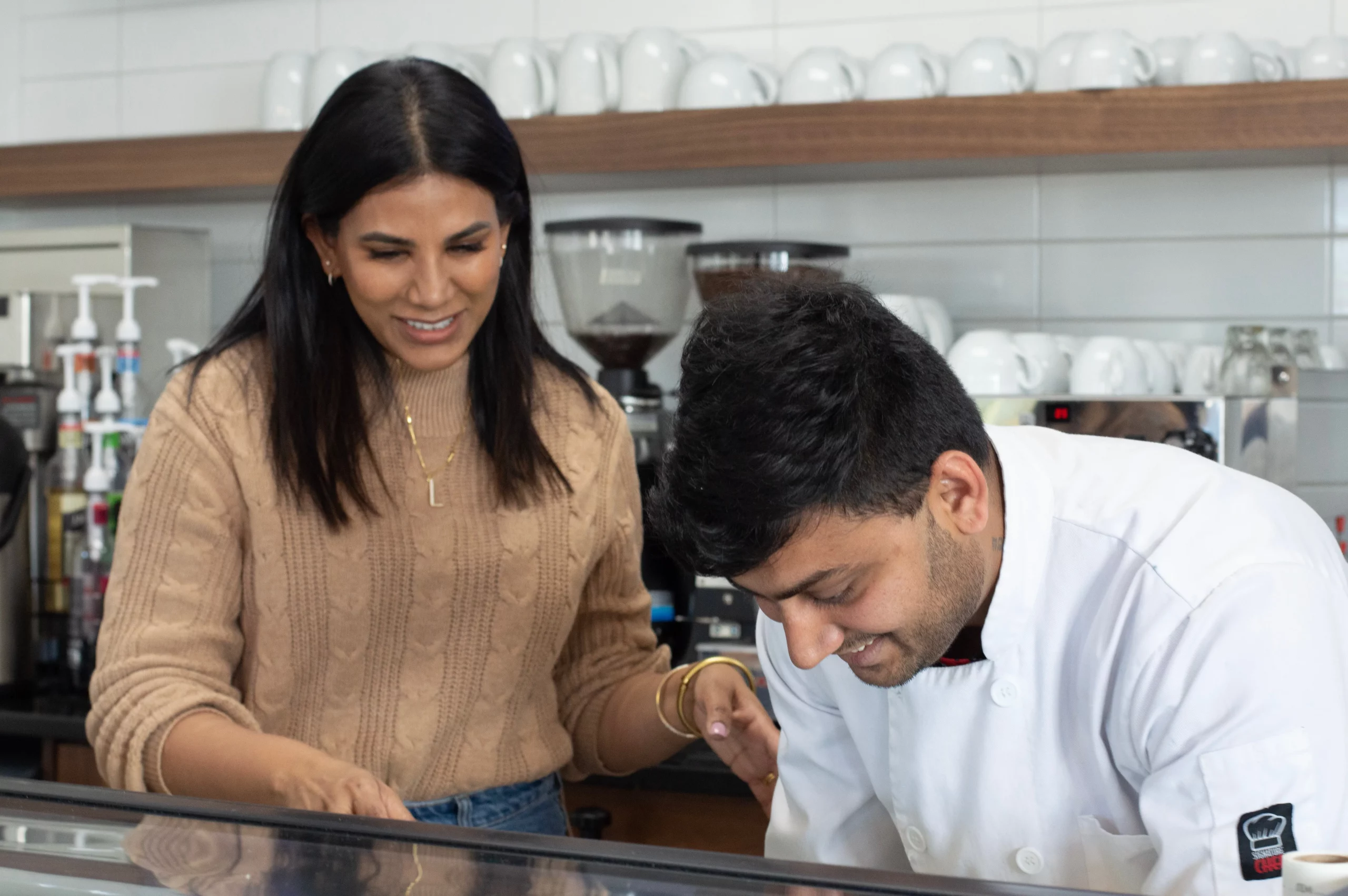 Lavanya Mahate and a chef smile while working in a kitchen together.