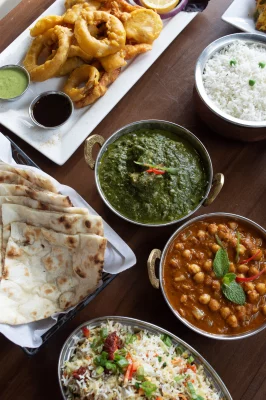 On a dark wooden table, an array of Indian dishes are laid out upon it.