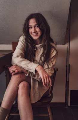 Stephe Clotele sits in a wooden chair, smiling at the camera.