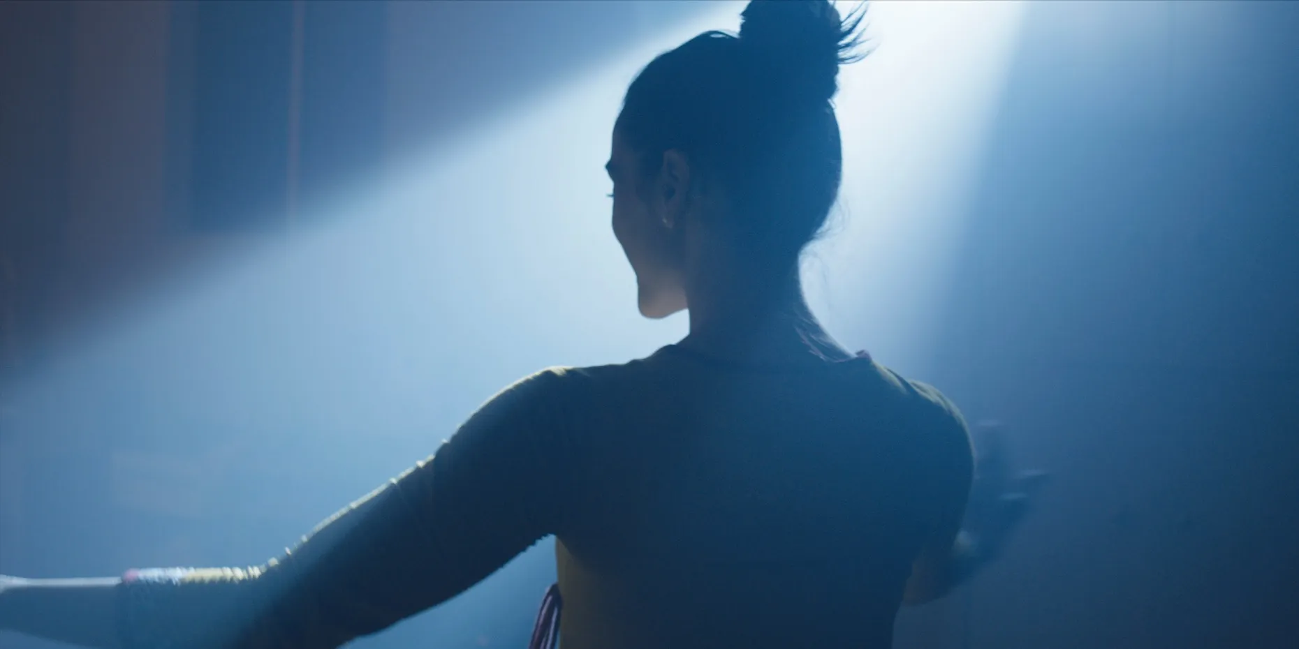 The back of a woman's head with her hair in a bun illuminated by blue light.