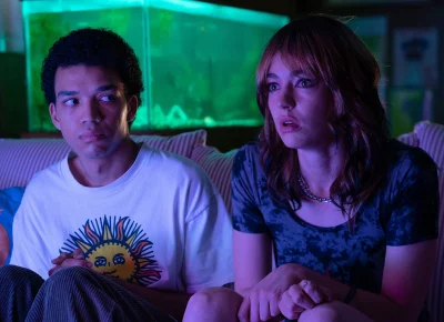 Two teenagers stare forward in a dark room.