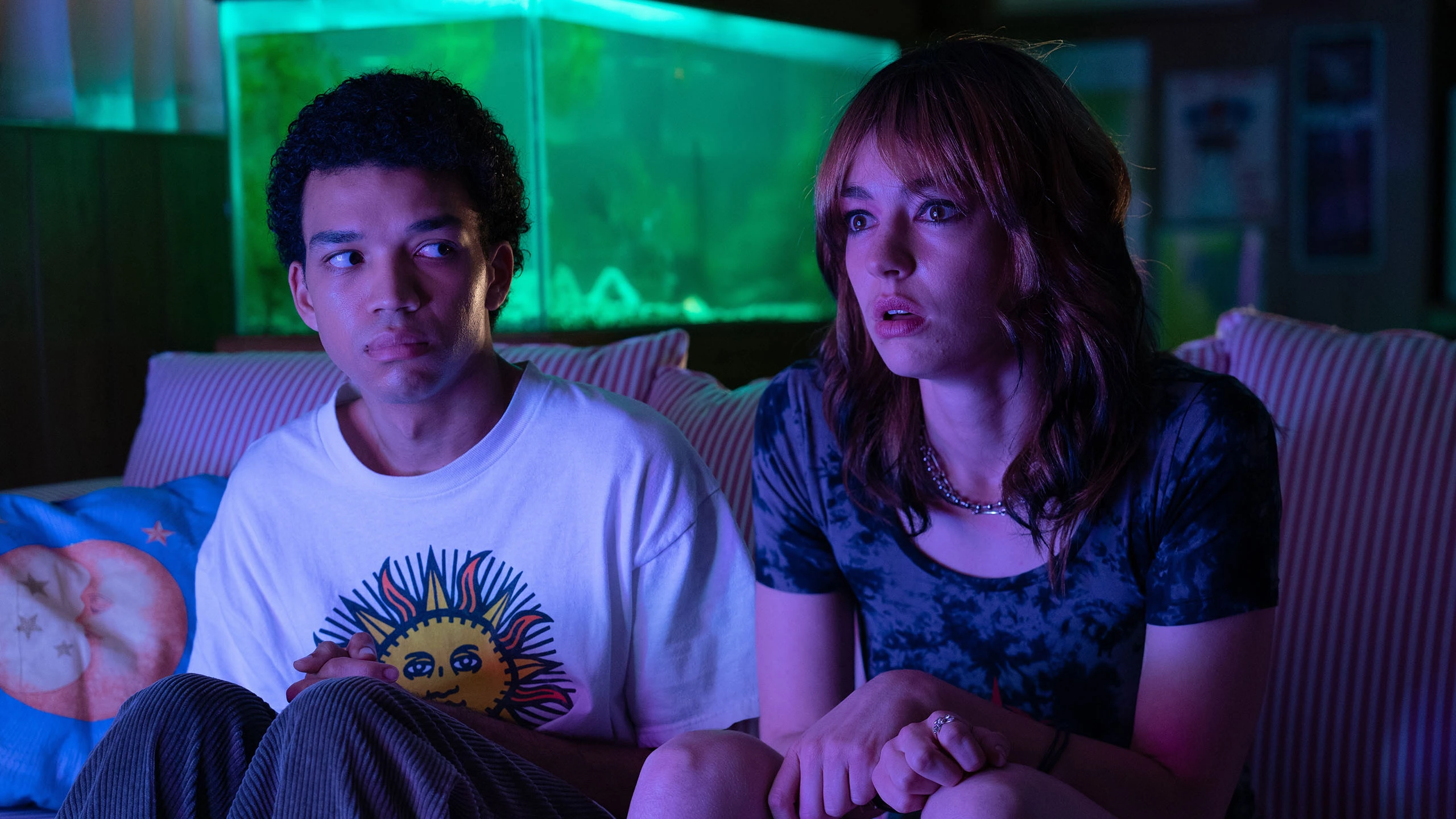 Two teenagers stare forward in a dark room.