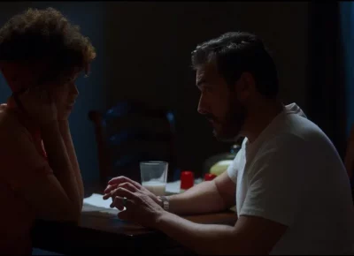 Two people are having a conversation over a table in a dimly lit room.