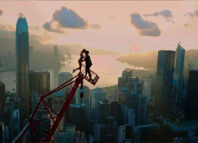 A couple kiss on a crane overlooking a city skyline.