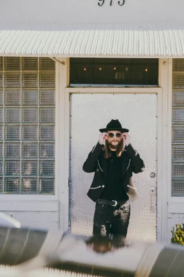 Graveljaw Keaton stands in front of a white door wearing sunglasses.