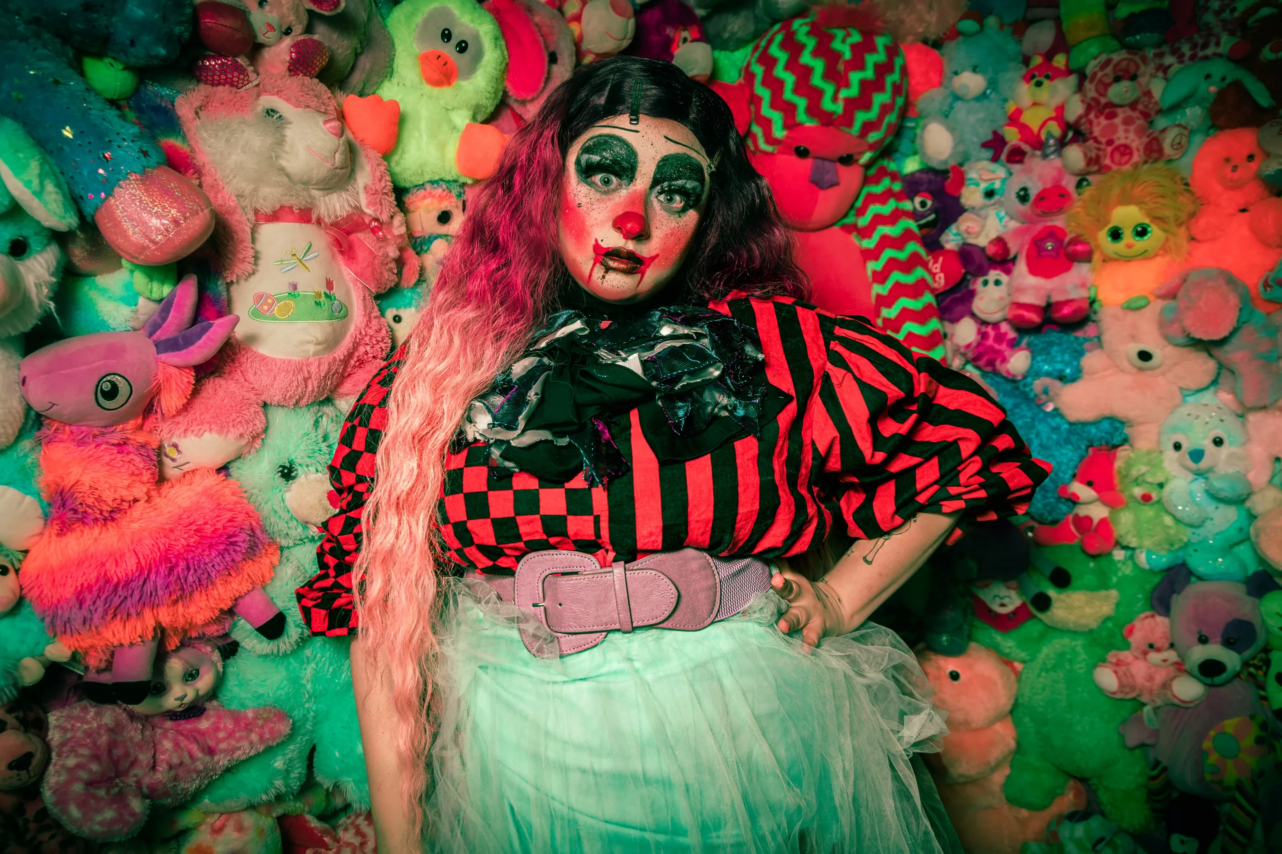 Shortcake the Clown stares at the camera in front of a wall of stuffed animals.