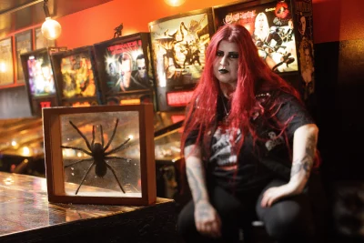 Emily Ard sits next to pinball machines with a framed spider in front of her. 