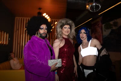Three drag queens stand smiling in Blue Gene's.