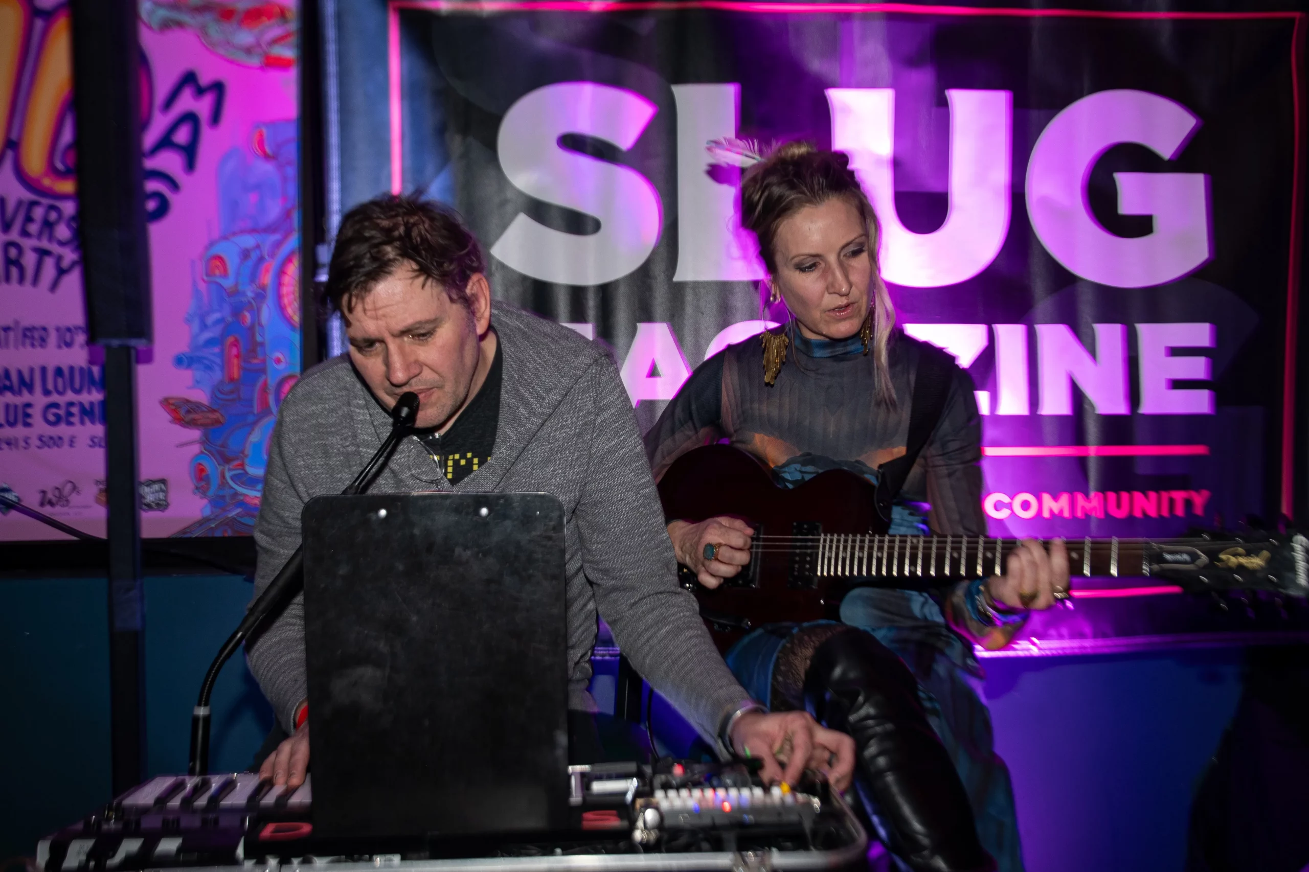 Angela H. Brown plays the guitar with Salt Lake City Demons in front of a SLUG Magazine banner.