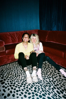 Alison Mosshart and Jamie Hince smile at the camera, sitting on a spotted rug.