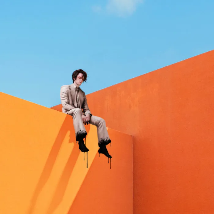 A person wearing a suit sits on top of an orange wall.