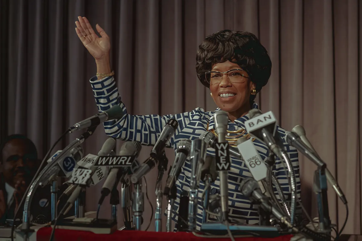 A woman waves at a podium to a bunch of reporters