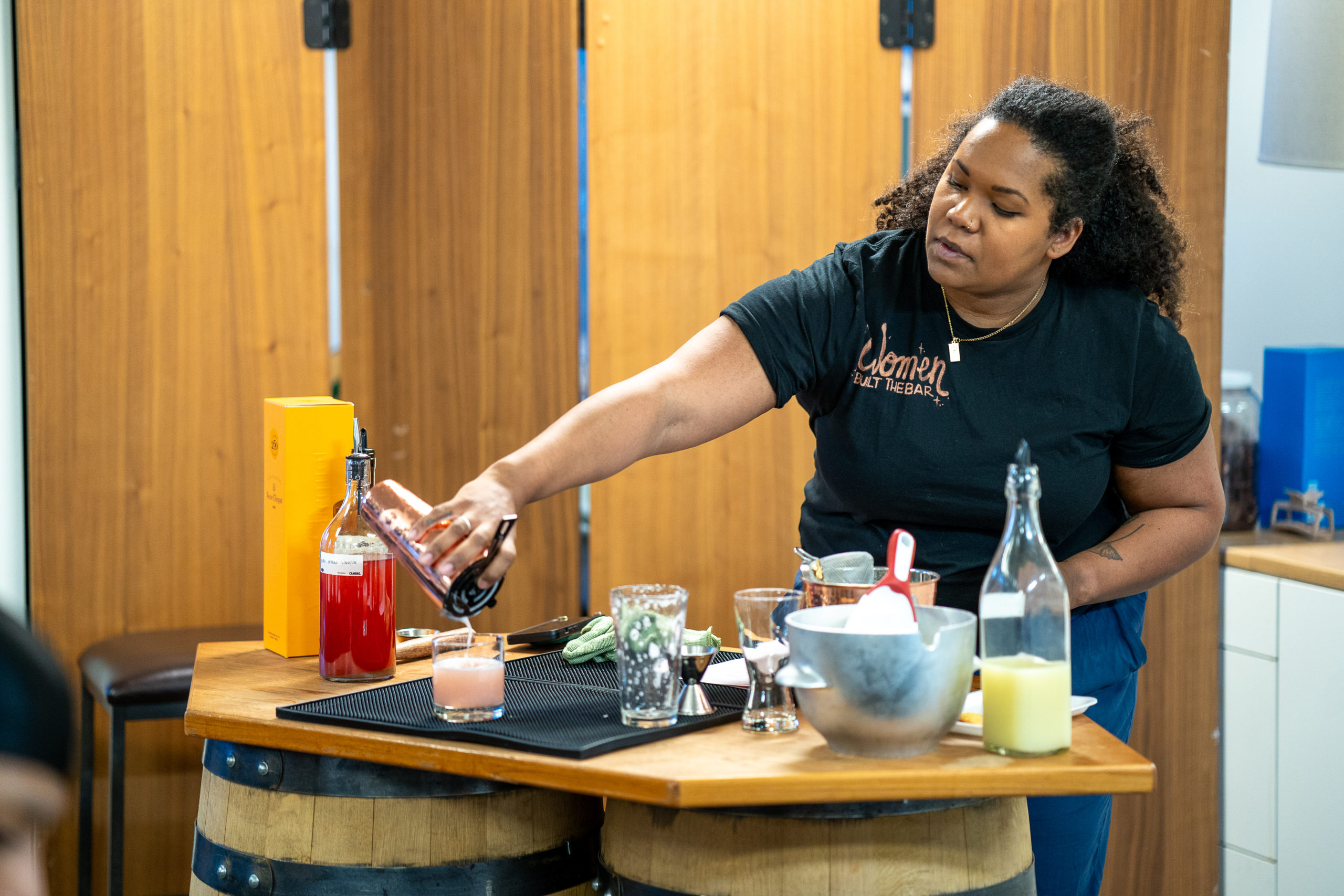 A woman pours a cocktail into a glass.