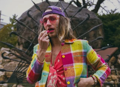 Bly Wallentine applyss lipstick while wearing a colorful outfit.