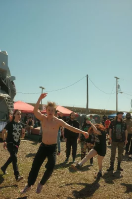 A shirtless man jumps around in a crowd outdoors. 