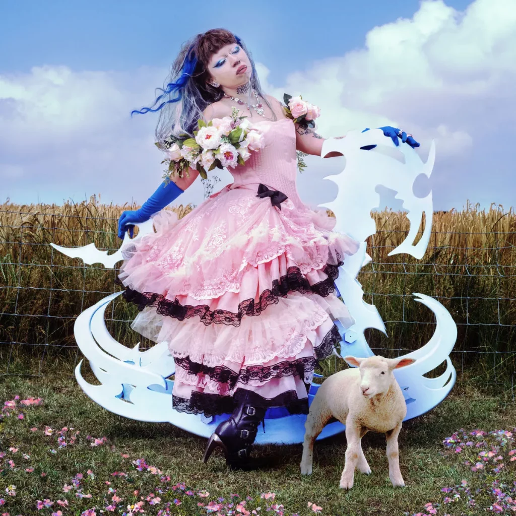 A woman in a flow-y tiered pink gown twirls in a fresh cut field. A lamb stands in front of her.