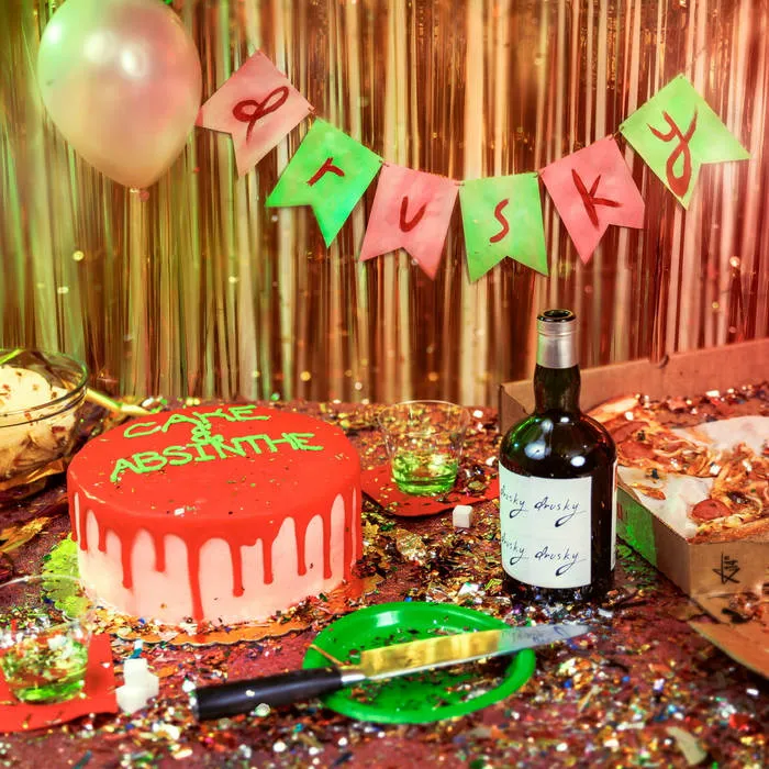 Party scene with cake and champagne bottle sitting on a table and a banner labeled "Drusky" behind it.
