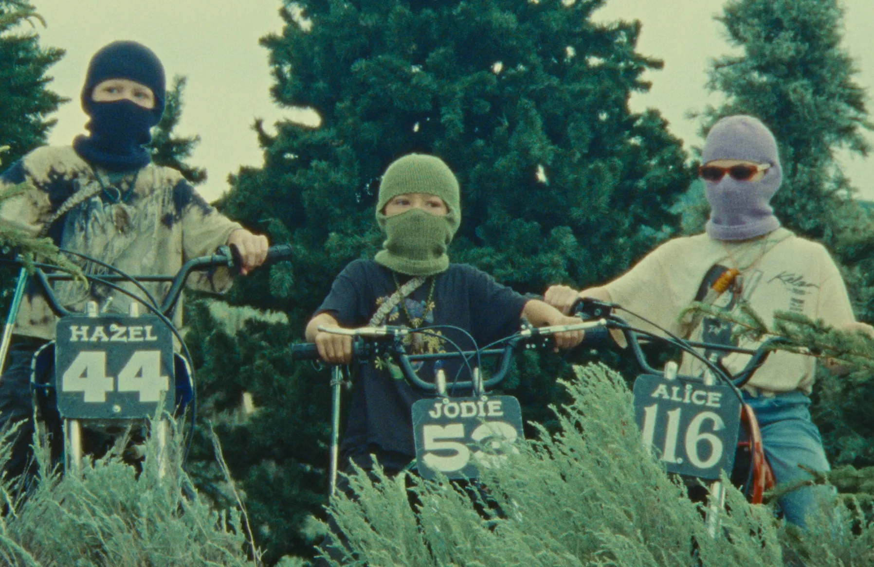 Three kids of various heights, in various knit balaclavas, sit on motorbikes.