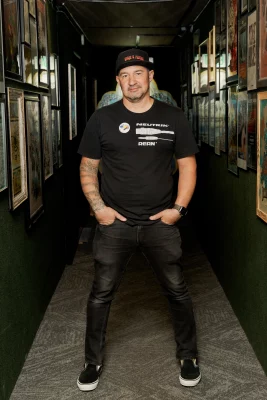 Charles Thorpe of Space and Faders recording studio stands in a dark green hallway decorated with framed album covers.