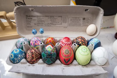 A dozen intricately designed eggs sit inside of an egg carton. 