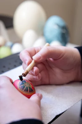 A stylus is held while painting a design on an egg.
