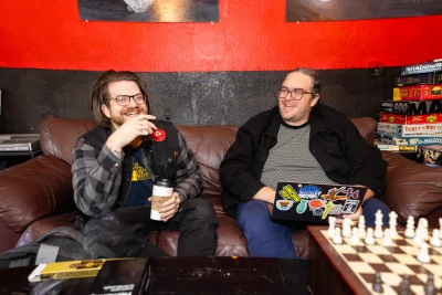 Atkin & Earley laugh on a couch in front of a chess set