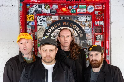 The band Gracemaker standing in front of a door covered in stickers.