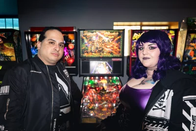Two people standing in front of pinball machines.