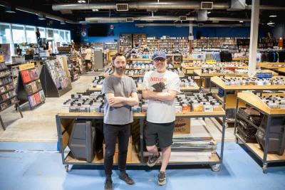 The owners of Graywhale pose with their arms crossed in front of rows of CDs